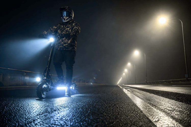Silhouette of a person riding an electric scooter on a dark, foggy road at night, illustrating the need for visibility and wireless LED blinkers
