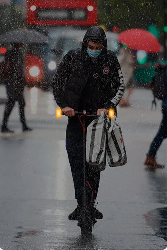 Electric scooter commuter using Ulip wireless LED turn signals in the rain for enhanced safety and visibility.