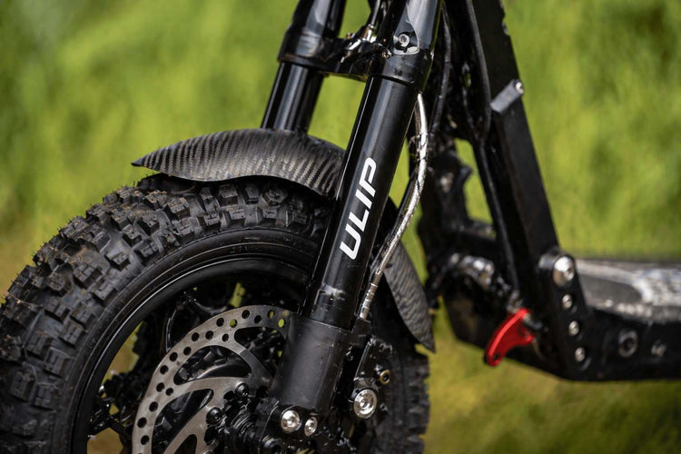 Close-up of a high-performance electric scooter equipped with Ulip rugged off-road tires and precision disc brake system, parked on a rock in an outdoor setting to showcase durability and suspension performance